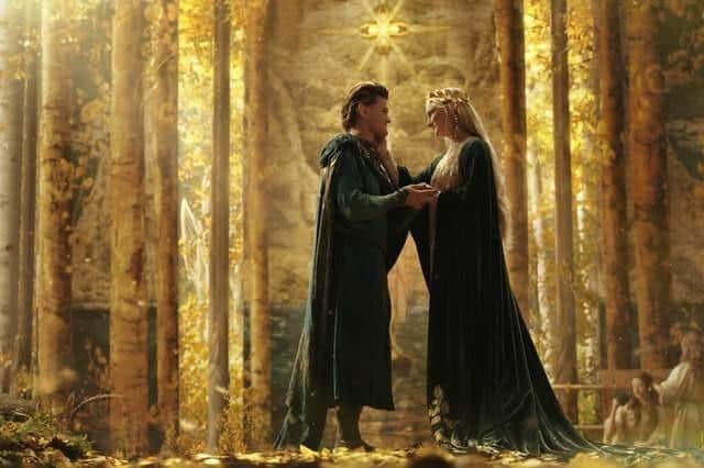 Robert Aramayo as Elrond and Morfydd Clark as Galadriel, embracing in a golden forest clearing. Picture: Ben Rothstein/Prime Video