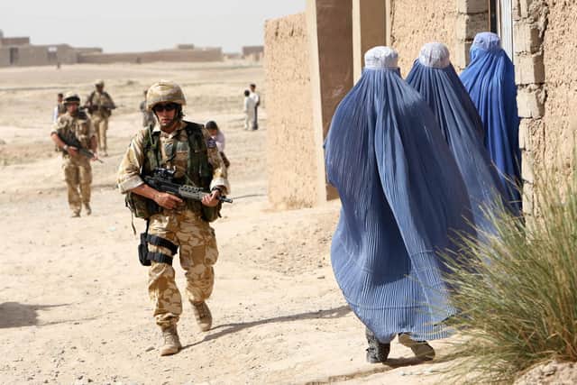 A British soldier walks past three women during a foot patrol in Lashkar Gah, Helmand province, in May 2006 (Picture: John D McHugh/AFP via Getty Images)