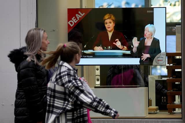 Passers-by look at a tv screen in a Glasgow shop showing First Minister Nicola Sturgeon making a Covid-19 statement during a virtual sitting of the Scottish Parliament. Picture date: Wednesday December 29, 2021.