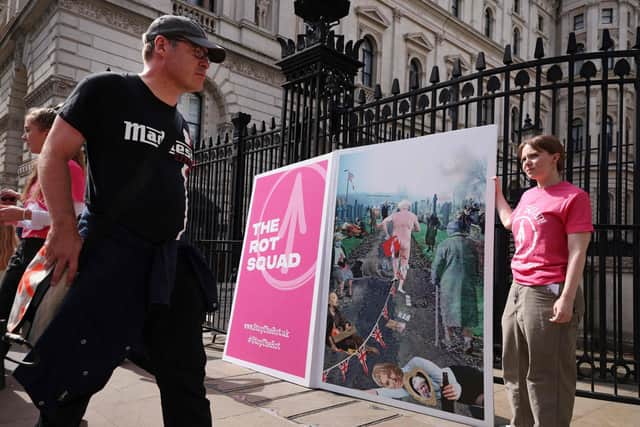 Demonstrators stand with a giant leaving card, depicting an image of Boris Johnson running away, outside of the entrance to Downing Street