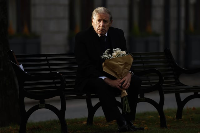A man looks on from a bench with a bouquet of flowers as he waits to view the cortege in Ballater (Photo by Jeff J Mitchell/Getty Images)