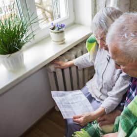 File photo of elderly couple in front of a heating radiator, holding an energy bill. Picture: Solarisys - stock.adobe.com