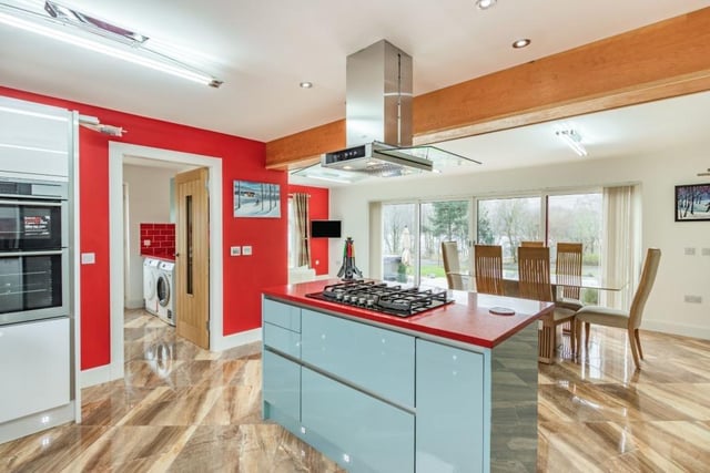Kitchen with range of contemporary high-gloss units, large central island with breakfast bar, modern integrated appliances including wine chiller, breakfast area, and French doors to the garden terrace.