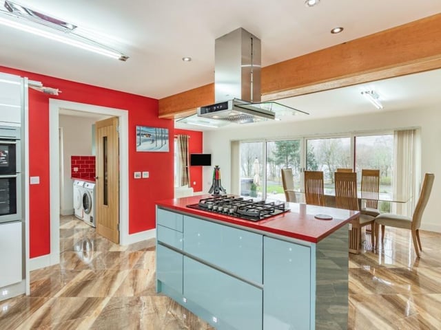Kitchen with range of contemporary high-gloss units, large central island with breakfast bar, modern integrated appliances including wine chiller, breakfast area, and French doors to the garden terrace.