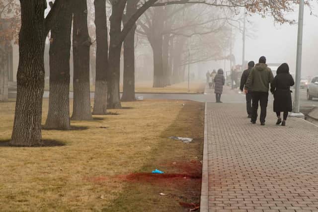People walk past blood on a curbside lawn in central Almaty on January 6, 2022, after violence that erupted following protests over hikes in fuel prices. Photo: ALEXANDER BOGDANOV/AFP via Getty Images.