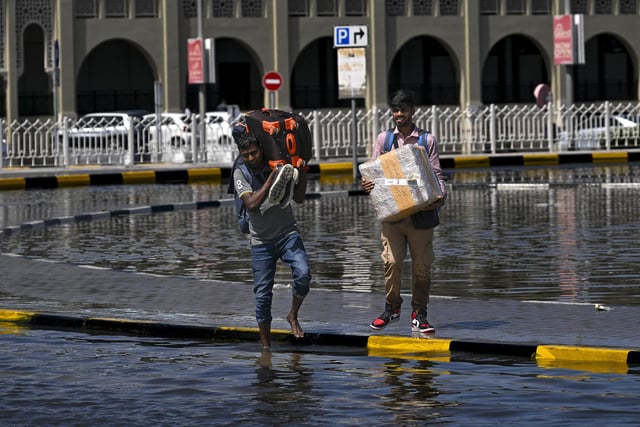 Men prepare to cross a flooded street following heavy rains in Sharjah, UAE, where there has been the worst rainfall in history.