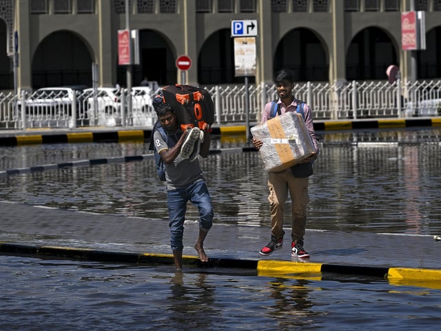 Men prepare to cross a flooded street following heavy rains in Sharjah, UAE, where there has been the worst rainfall in history.