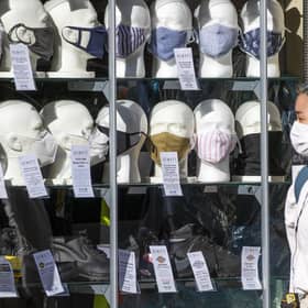 A woman wearing a protective face mask walks past a shop selling masks in Edinburgh city centre