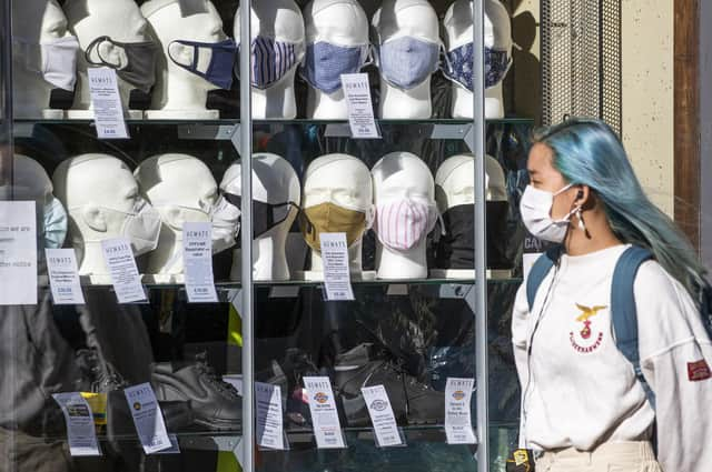 A woman wearing a protective face mask walks past a shop selling masks in Edinburgh city centre