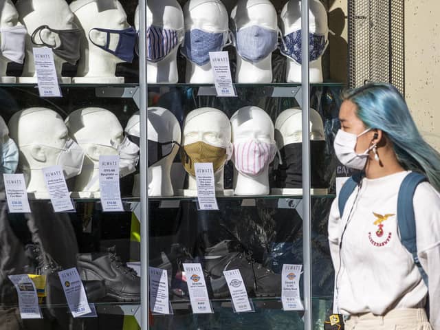 A woman wearing a protective face mask walks past a shop selling masks in Edinburgh city centre