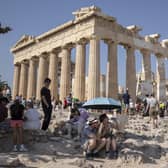 A tourist drinks water as she and a man sit under an umbrella in front of the five century BC Parthenon temple at the Acropolis hill during the heatwave. Picture: AP Photo/Petros Giannakouris