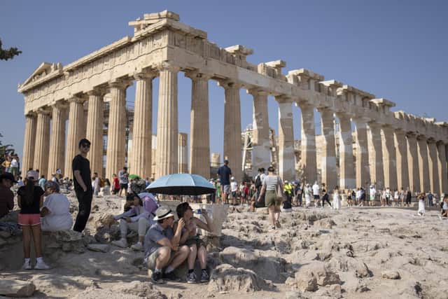 A tourist drinks water as she and a man sit under an umbrella in front of the five century BC Parthenon temple at the Acropolis hill during the heatwave. Picture: AP Photo/Petros Giannakouris