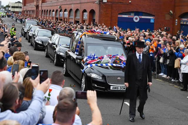 The funeral director leads the way as crowds gather on both sides of the road.