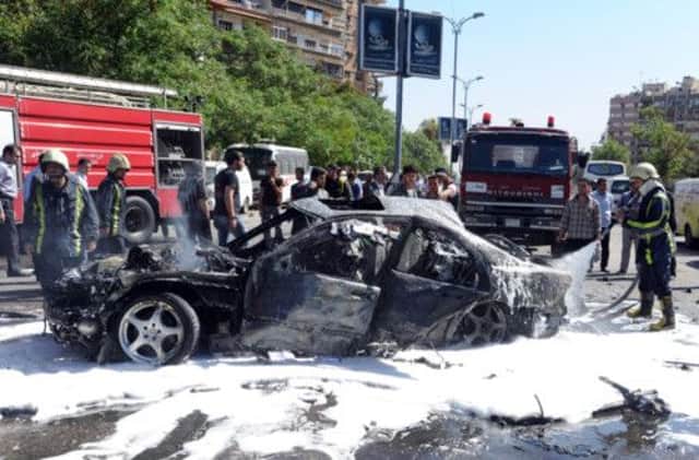 Fire crews deal with the smouldering wreckage of one of the cars targeted in yesterdays bombing in Damascus. Picture: AP