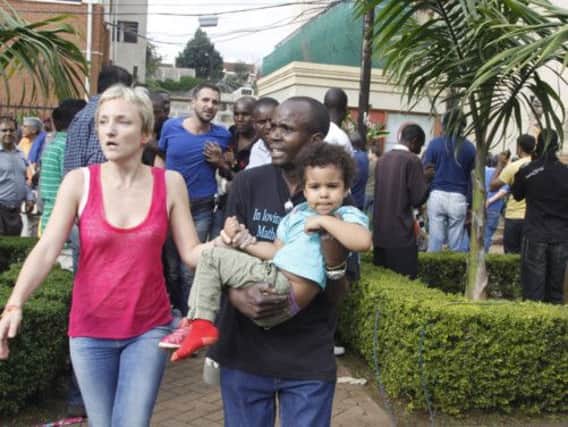 A traumatised mother and a child are helped to flee the upmarket mall by a security guard. Picture: AP
