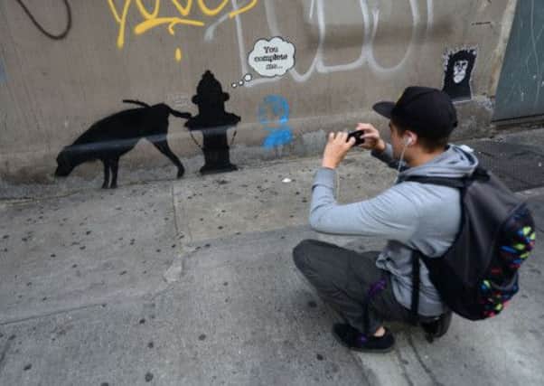 A man takes a photo of street graffiti by British artist Banksy in New York. Picture: Emmanuel Dunant/Getty