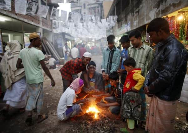 A fire is a welcome source of warmth on Dhakas streets, lined with campaign posters. Picture: Reuters