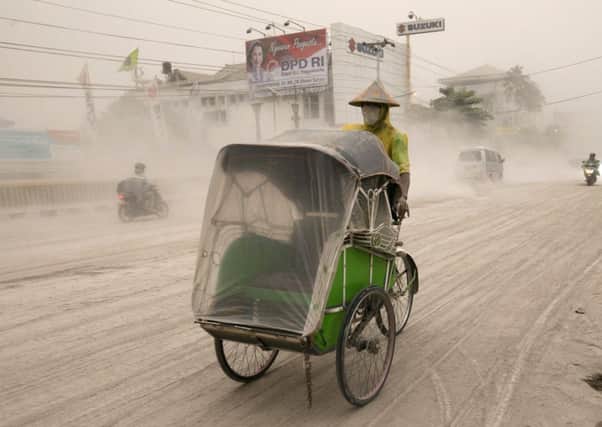 A man wears a mask as he rides a becak, a kind of rickshaw, on a road covered with from Mount Kelud,  in Yogyakarta. Picture: Reuters