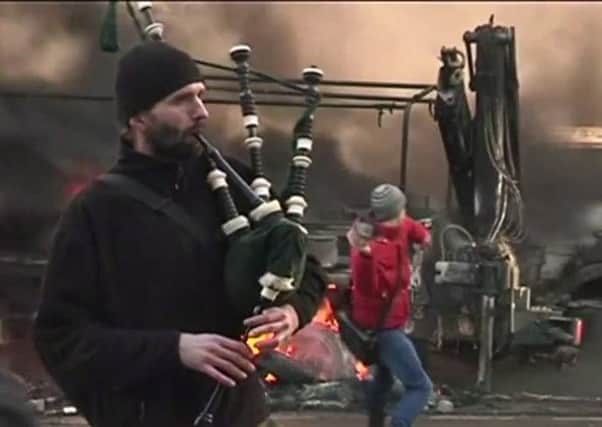 The man plays his bagpipes while a protester in the background hurls a missile. Picture: YouTube