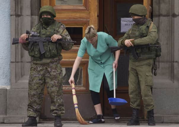 A woman sweeps away broken glass as two unidentified armed men guard the local government building in Simferopol. Picture: AP