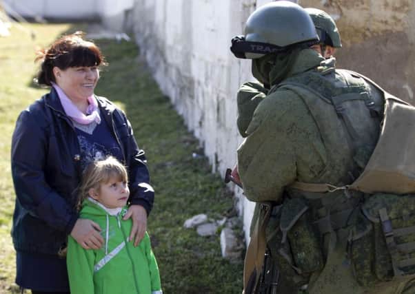 A Ukrainian girl looks at military personnel, believed to be Russian servicemen, standing outside the territory of a Ukrainian military unit in the village of Perevalnoye. Picture: Reuters