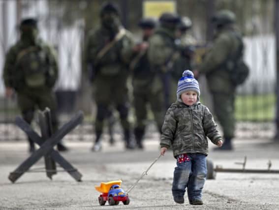 A child drags a toy past pro-Russian soldiers standing outside a military base in Perevalne, Crimea. Picture: AP