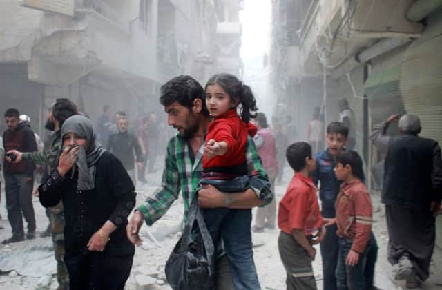 A man carrying a child makes his way through rubble after reported air strikes by government forces. Picture: AFP