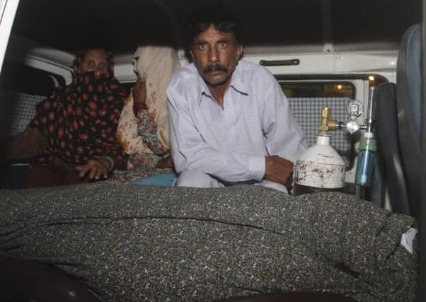 Mohammad Iqbal, right, husband of Farzana Parveen, 25, sits in an ambulance next to the body of his pregnant wife who was stoned to death. Picture: AP