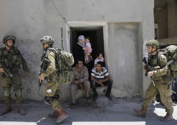 Palestinians sit outside their house as Israeli soldiers patrol their street near Hebron. Picture: Reuters