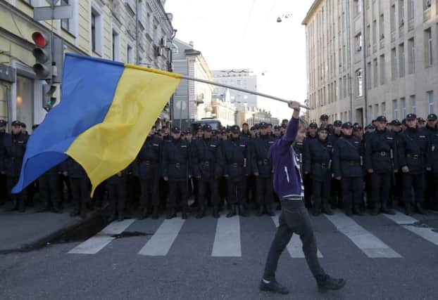 A young man with a Ukrainian flag walks defiantly past riot police in Moscow. Picture: Reuters