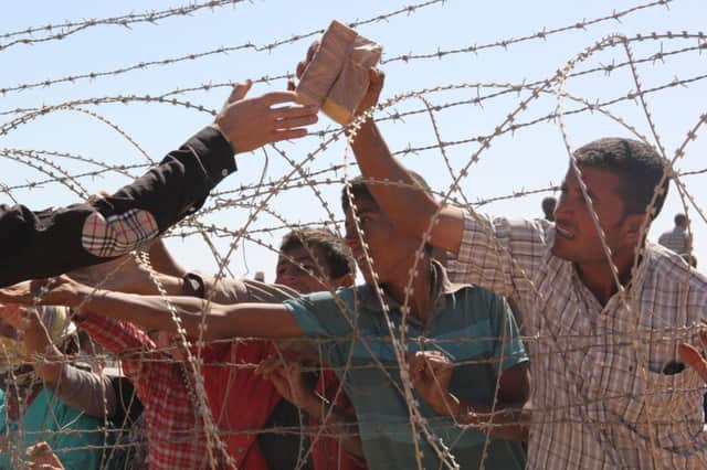 A Turkish man passes food supplies across a fence to Syrians gathering on the border. Picture: Getty