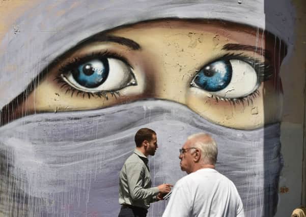 People walk past a mural of a Muslim woman painted on a wall in an inner city suburb in Sydney. Picture: Getty