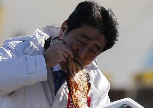 Japans Prime Minister Shinzo Abe, on the election trail, tries some grilled fish. Picture: Reuters