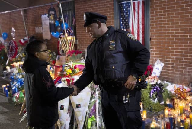 A boy shakes the hand of a NYPD officer at a makeshift, floral shrine to Eric Garner in New York. Picture: John Minchillo/AP Photo