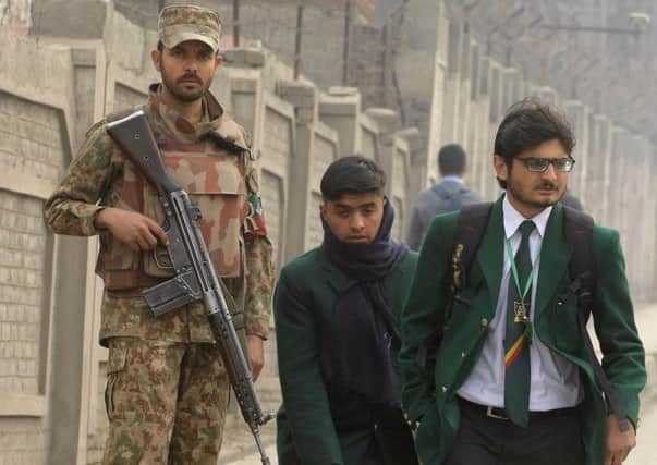 Students walk past a soldier on guard outside the school in Peshawar, where Taleban gunmen killed 150 people. Picture: AP