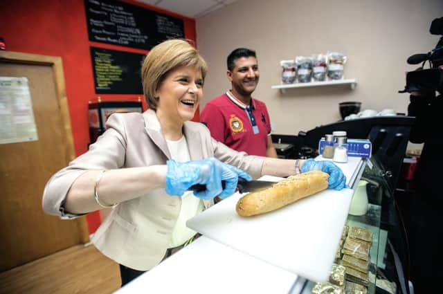 The First Minister helps deli owner Aftab Baig yesterday in Glasgow Central. Picture: Wattie Cheung