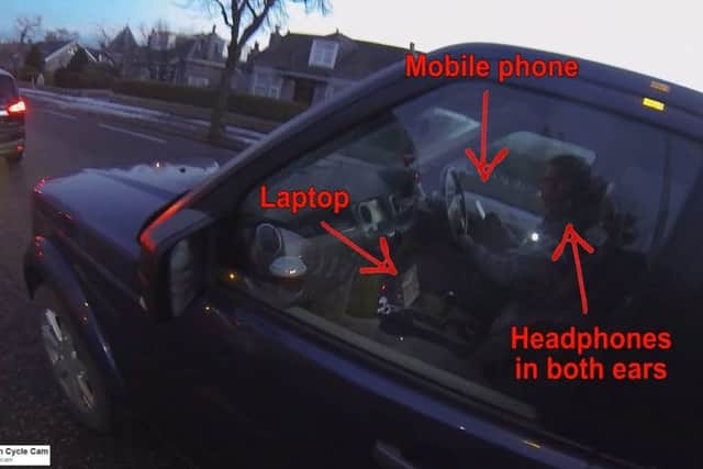The driver was caught on camera driving down a busy street while holding a mobile phone, watching a video and wearing earphones. Picture: SWNS