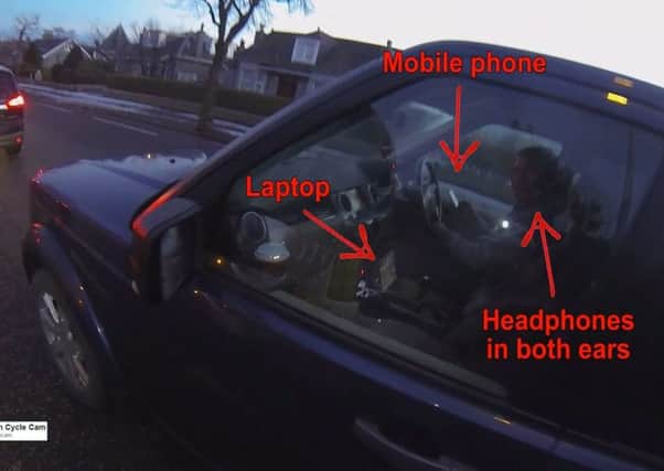 The driver was caught on camera driving down a busy street while holding a mobile phone, watching a video and wearing earphones. Picture: SWNS