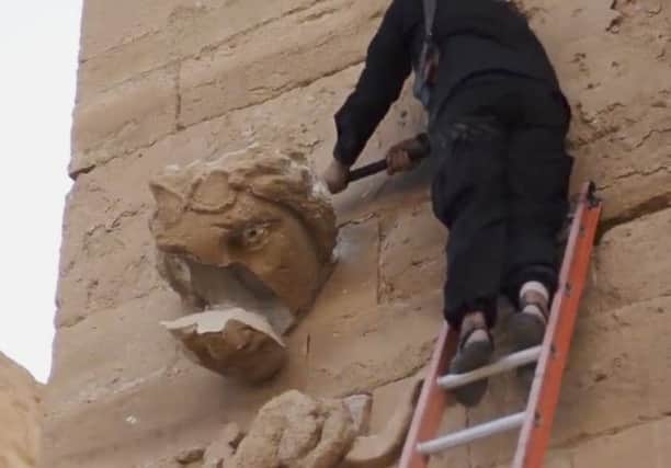 A piece falls off from a curved face on the wall of an ancient building as a militant hammers it in Hatra. Picture: AP