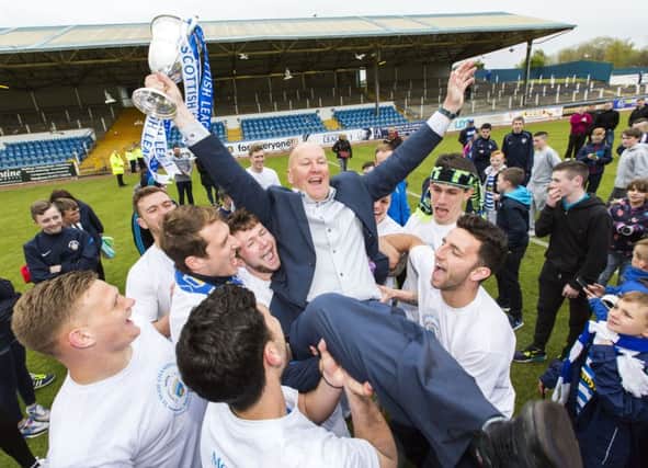 Morton manager Jim Duffy raises the League 1 trophy as his players hold him aloft. Picture: SNS