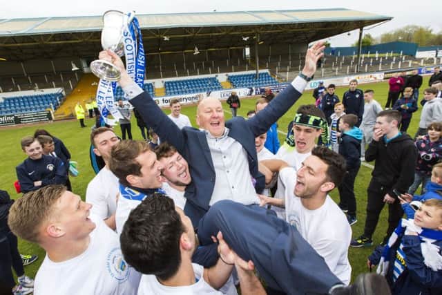 Morton manager Jim Duffy raises the League 1 trophy as his players hold him aloft. Picture: SNS