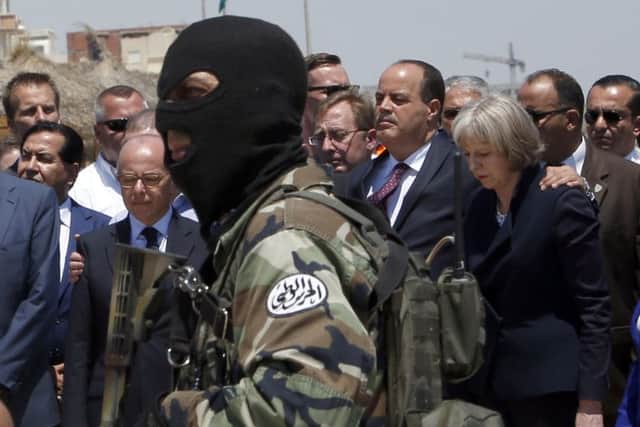 A Tunisian police officer stands guard as British Home Secretary Theresa May, right, Tunisian Interior Minister Mohamed Najem Gharsalli, second right, and French Interior Minister Bernard Cazeneuve, left, pay respect to the victims of Friday's shooting. Picture: AP
