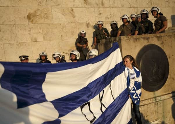 Supporters of the NO vote in the upcoming referendum hold a Greek flag as riot police block the entrance of the parliament. Picture: AP