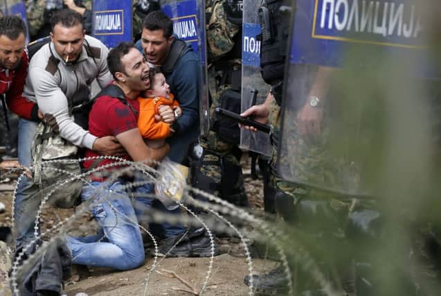 Migrants help a man and boy as they are stuck between Macedonian riot police officers and fellow migrants. Picture: AP