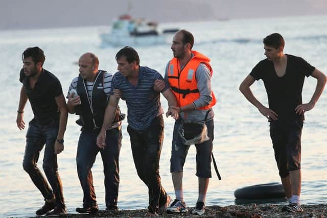 Overcome with exhaustion after swimming the final 50 yards of his journey, a migrant from Syrial, centre, is helped to shore on the island of Kos. Picture: Getty Images