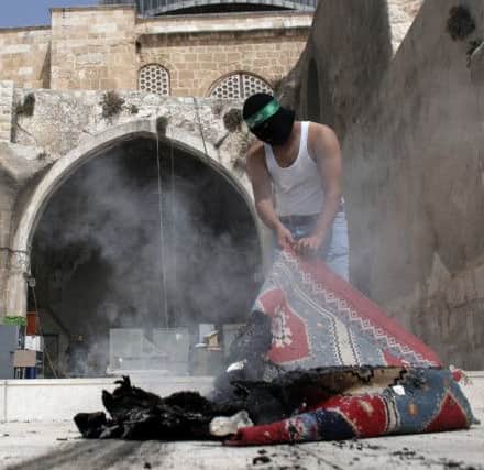A Palestinian wearing a Hamas headband takes a burnt carpet out of Al-Aqsa mosque yesterday. Picture: Getty