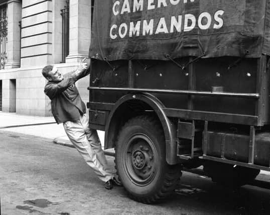 Actor and comedian Spike Milligan hangs on to the back of a Cameron's Commandos truck outside the Alhambra Theatre in July 1967. Picture: TSPL
