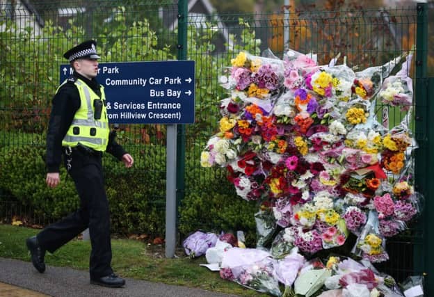 A police officer walks past floral tributes left outside Cults Academy. Picture: PA