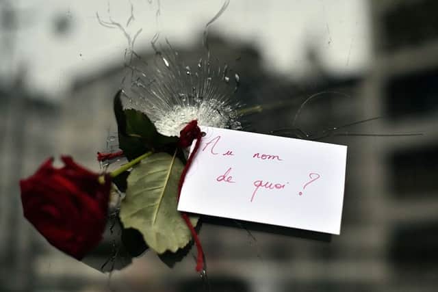 A rose with a sign reading 'In the name of what?' is pictured in a bullet hole in a restaurant window. Picture: AFP/Getty Images