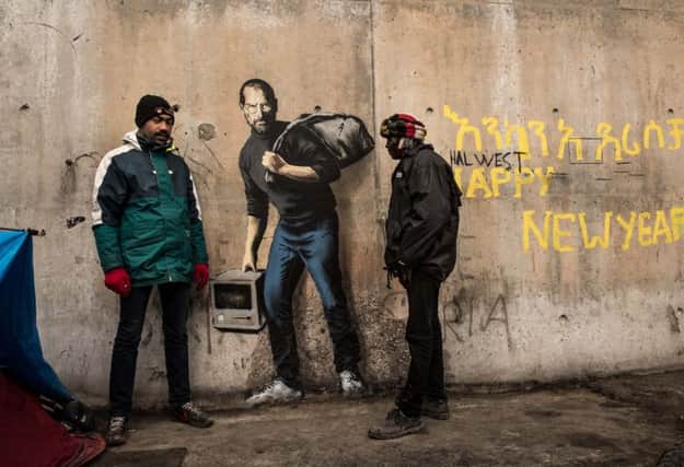Two men stand next to a street art graffiti by elusive British artist Banksy representing Steve Jobs. Picture: Getty Images